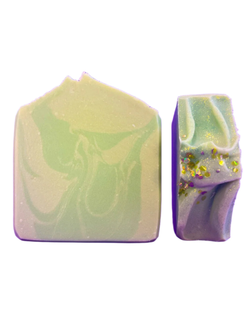 Two swirled soap bars, one green and white, the other purple and white with specks, on a white background.
