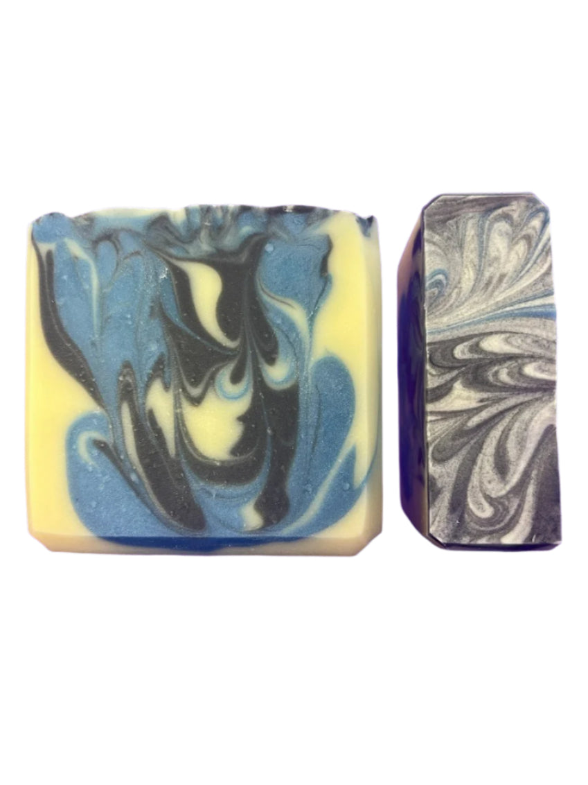 Two marbled soap bars, one with blue, black, and yellow swirls, the other with gray and white swirls, on a white background.