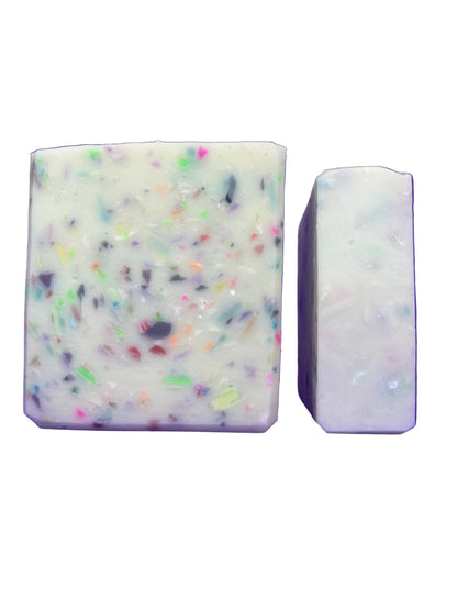 Two bars of soap, one with colorful specks and the other plain, on a white background